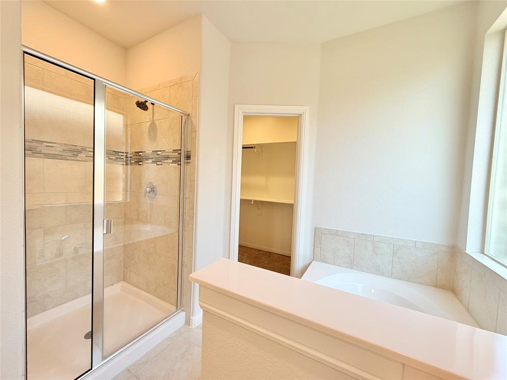 Walk-in shower with glass enclosure and tile surround featuring decorative stone-finish accents, deep soaking tub with tile surround, and built-in closet shelving
