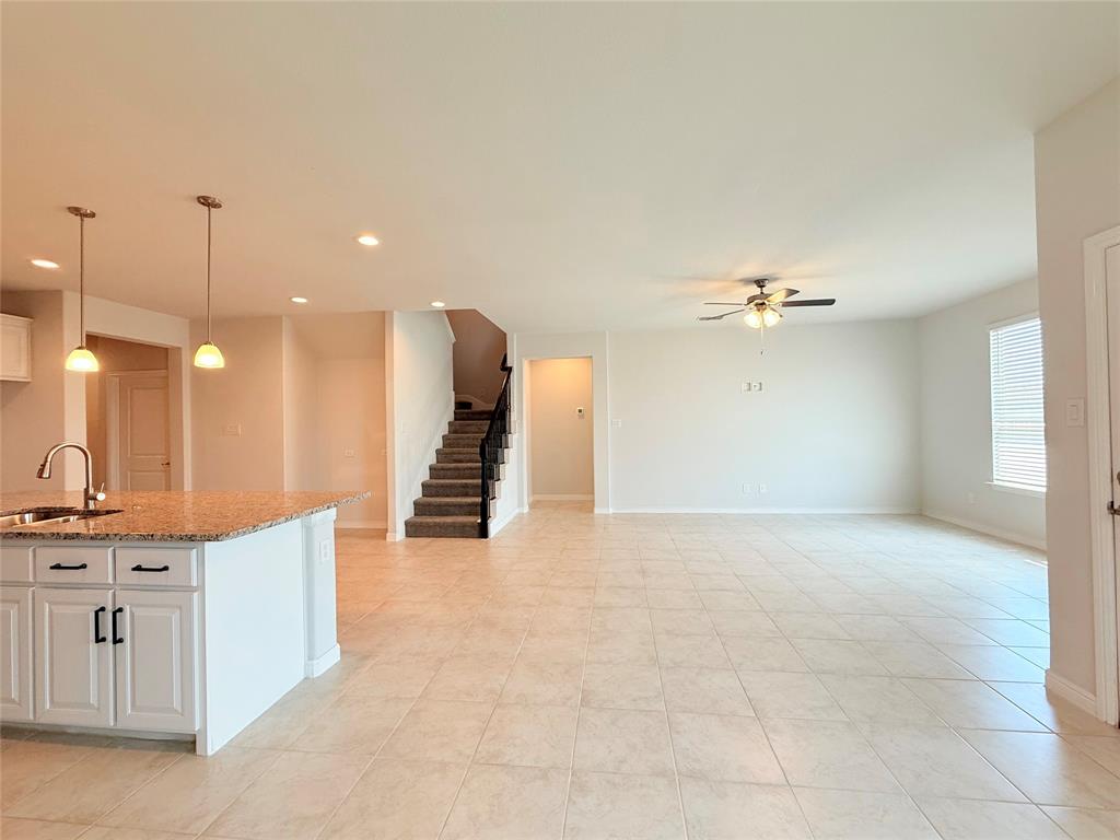 Kitchen featuring a stone-surface island, white shaker-style cabinetry, and dual pendant lighting, complemented by tile flooring, recessed lighting, and a staircase with a dark-finish balustrade