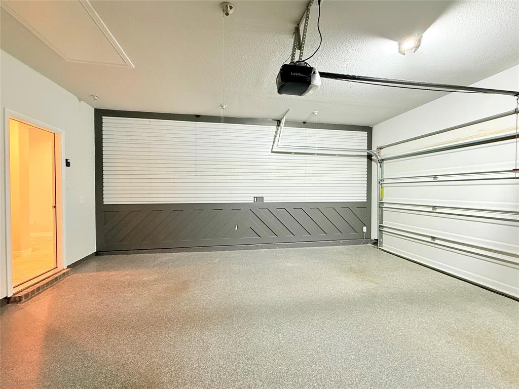 Garage featuring epoxy-coated flooring, decorative diagonal wainscoting, integrated wall organization slats, and an automatic door opener