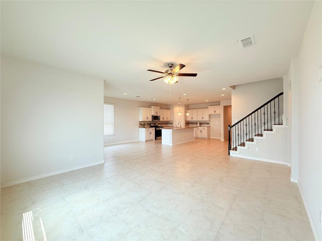 Open-concept floor plan featuring tile flooring, a kitchen island with built-in cabinetry, recessed lighting, and a staircase with wrought iron balusters