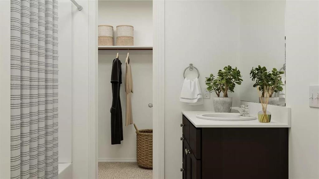 Bathroom featuring a dark-finish vanity with a white countertop and oval undermount sink, large wall-mounted mirror, brushed-nickel towel ring, and walk-in closet with built-in shelving