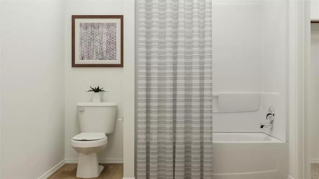 Full bathroom featuring a white porcelain toilet, a composite tub and shower surround, and polished chrome plumbing fixtures, complemented by wood-finish flooring