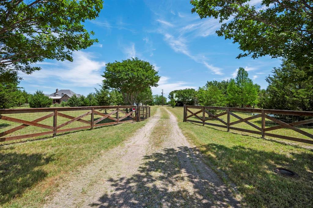 Gravel driveway leading to the property, framed by wood cross-buck fencing and mature trees