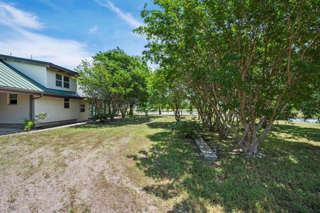 Exterior featuring horizontal siding, a green metal roof, expansive lawn, mature trees, and a concrete walkway