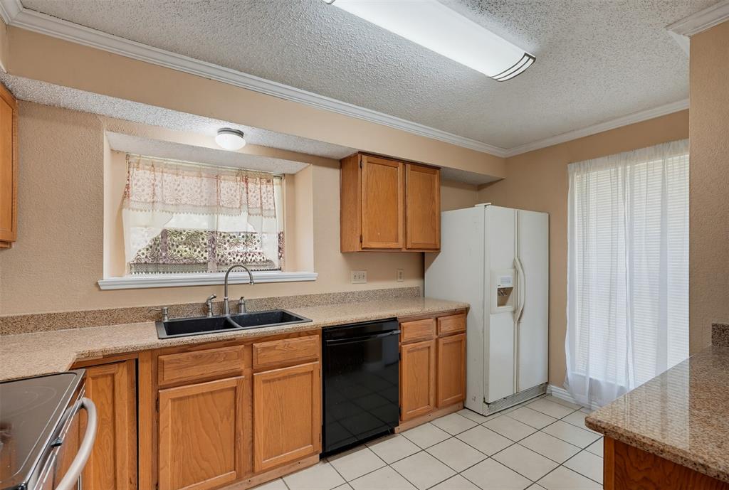 Kitchen featuring wood cabinetry, stone-finish countertops, dual-basin sink with arched faucet, ceramic tile flooring, and integrated lighting fixtures