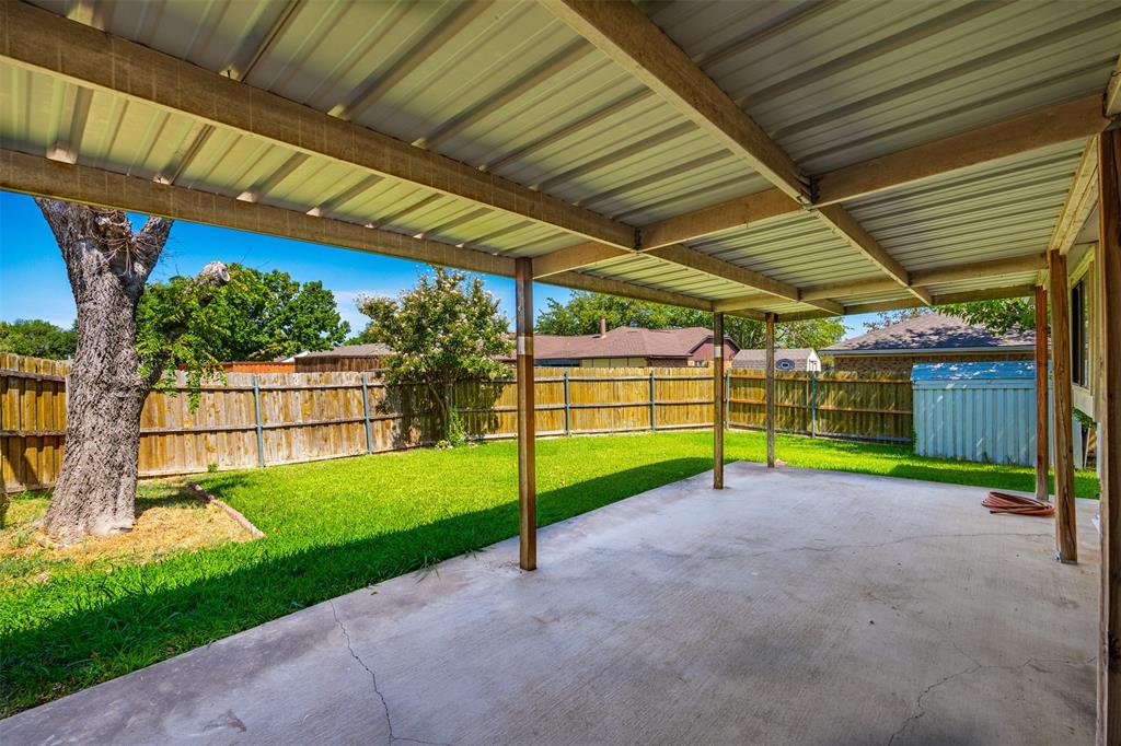 Covered concrete patio featuring a metal roof structure, wood-fencing enclosure, and lawn space