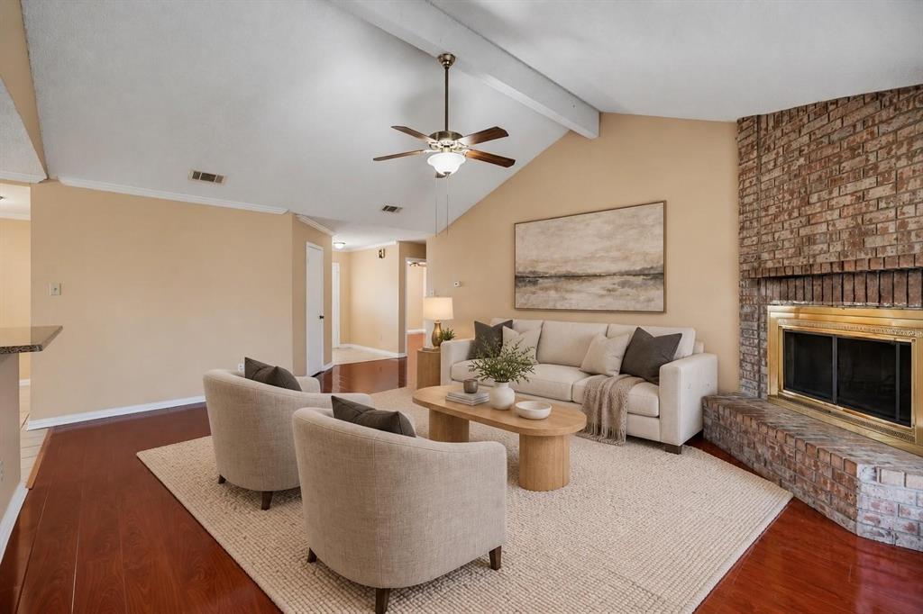 Living area featuring a vaulted ceiling with exposed beam, wood-finish flooring, and a floor-to-ceiling brick fireplace with a metal surround Living area featuring a vaulted ceiling with exposed beam, wood-finish flooring, and a floor-to-ceiling brick fireplace with a metal surround