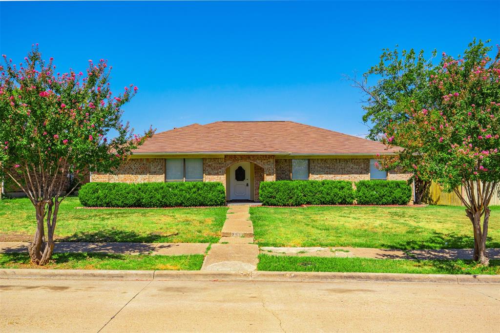 Single-story residence featuring a brick exterior, a hip roof, a recessed arched entryway, and manicured landscaping Single-story residence featuring a brick exterior, a hip roof, a recessed arched entryway, and manicured landscaping
