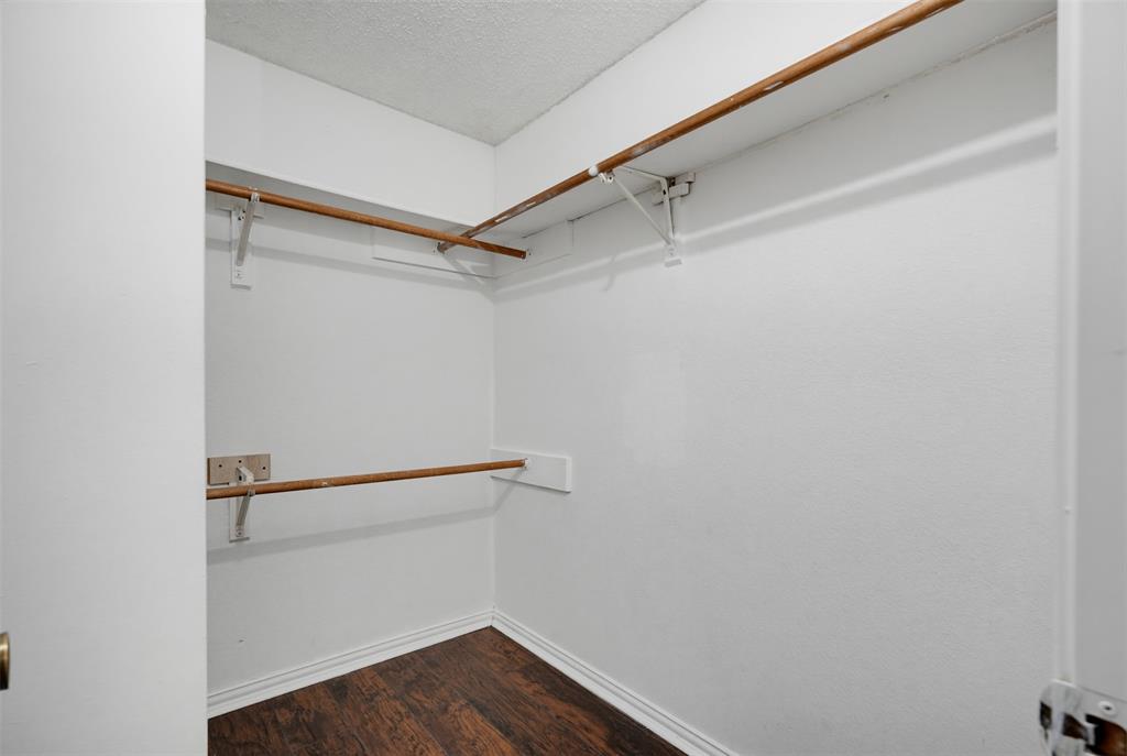 Walk-in closet featuring wood-finish flooring, dual-tier wood shelving, and metal support hardware