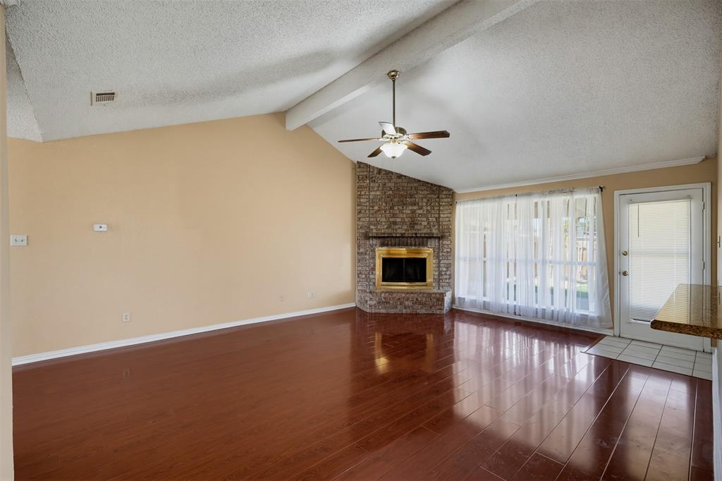 Living area featuring vaulted ceilings with exposed beams, wood-finish flooring, and a stone-clad corner fireplace with a metal surround Living area featuring vaulted ceilings with exposed beams, wood-finish flooring, and a stone-clad corner fireplace with a metal surround