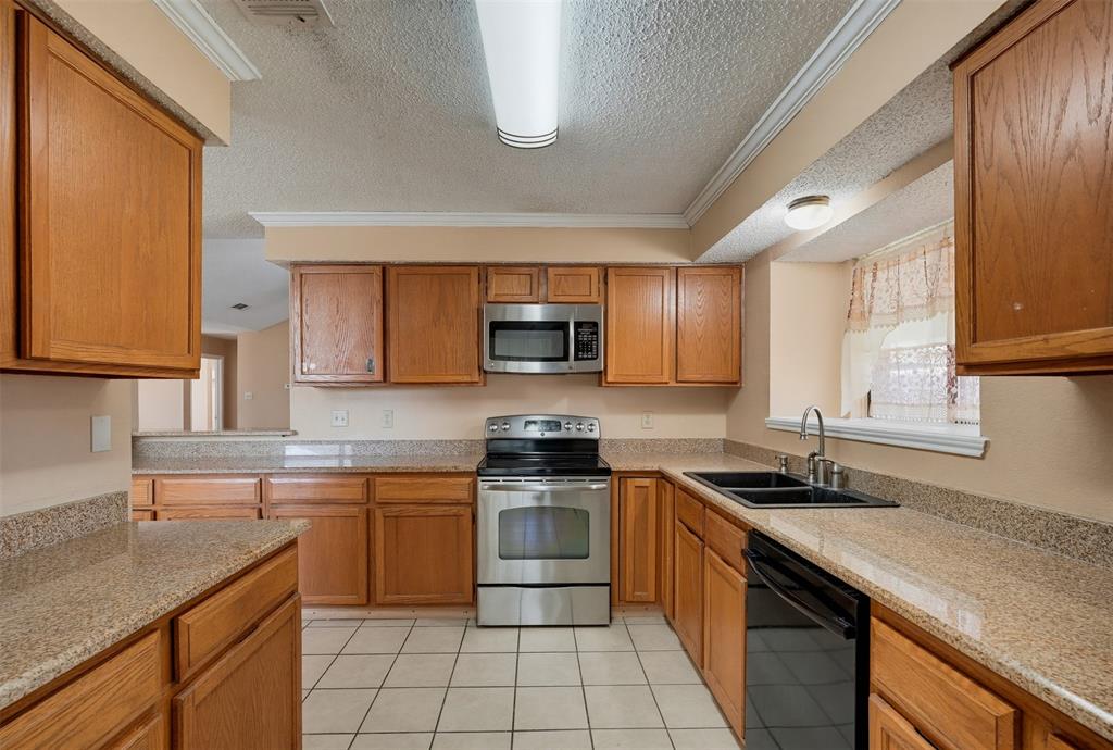 Kitchen featuring wood cabinetry, stone-surface countertops, stainless steel appliances, a double-basin sink, and tile flooring