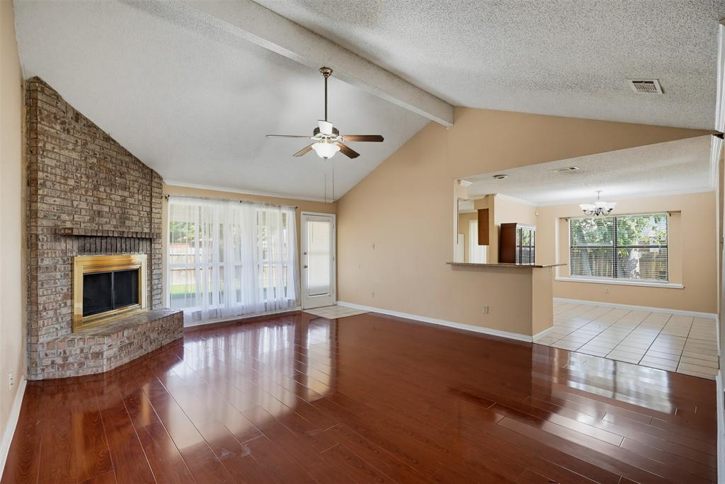 Vaulted ceilings with exposed structural beam, floor-to-ceiling brick fireplace, wood-finish flooring, and tile kitchen flooring featuring a breakfast bar