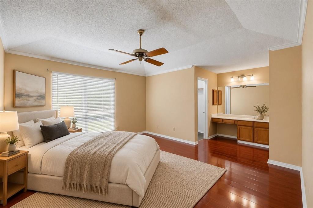 Vaulted ceilings, wood-finish flooring, ceiling fan with light fixture, large window with horizontal blinds, and a built-in vanity with cabinetry and oversized mirror