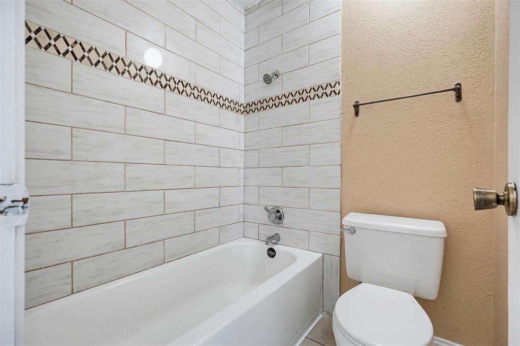 Bathtub with white ceramic subway-style wall tiling and decorative glass mosaic accent band, wall-mounted shower head, chrome plumbing fixtures, and white toilet