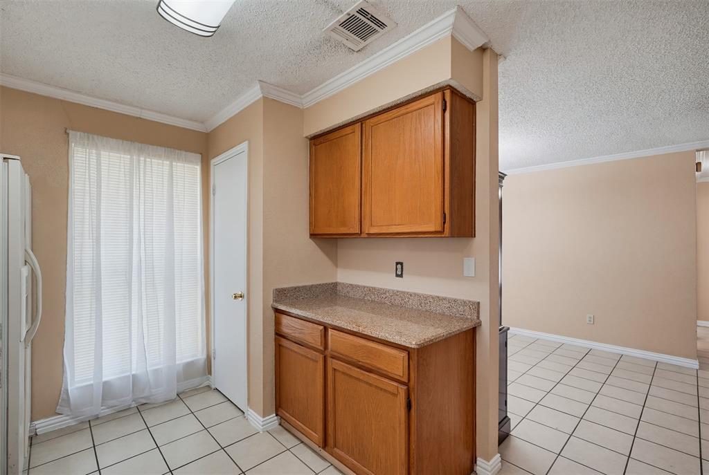 Wood cabinetry featuring upper and lower storage, stone-finish countertops, tile flooring, and crown molding