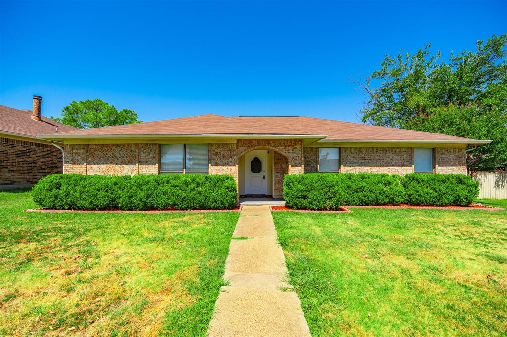 Single-story brick exterior featuring a shingled hip roof, arched entryway, and manicured shrubbery Single-story brick exterior featuring a shingled hip roof, arched entryway, and manicured shrubbery