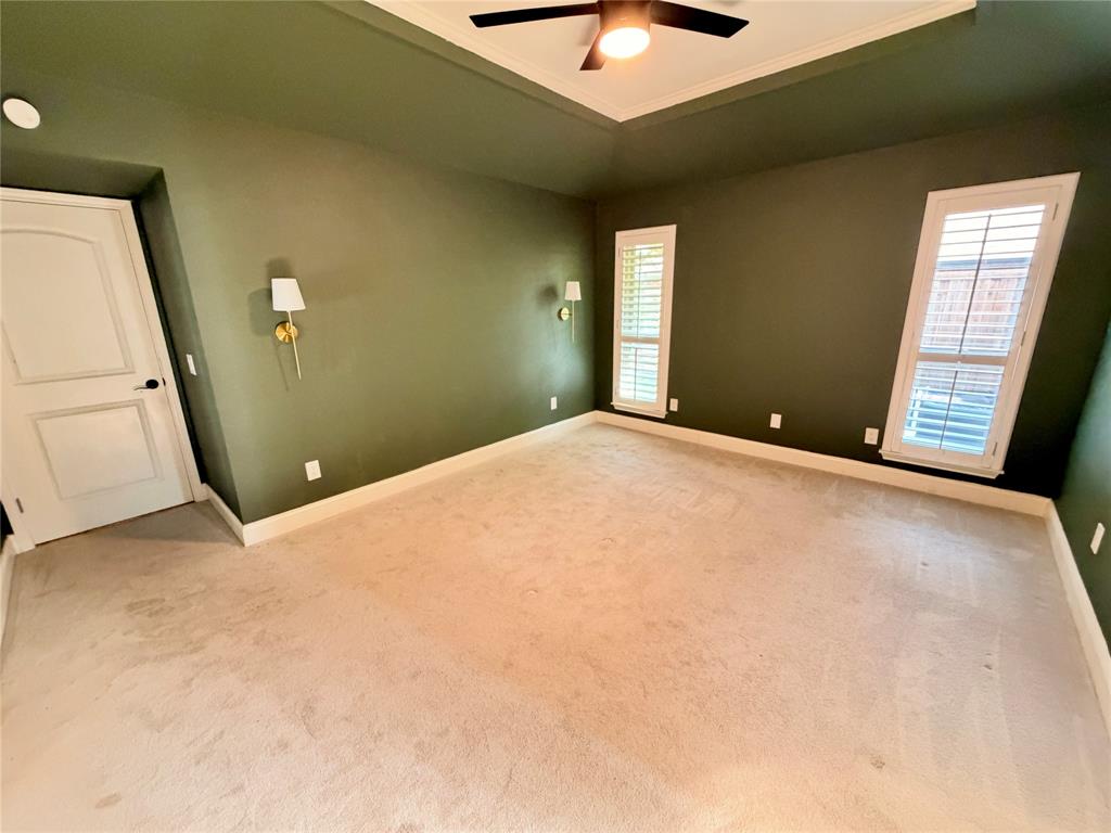 Tray ceiling featuring a central lighted ceiling fan, dual wall-mounted light fixtures, and white plantation shutters
