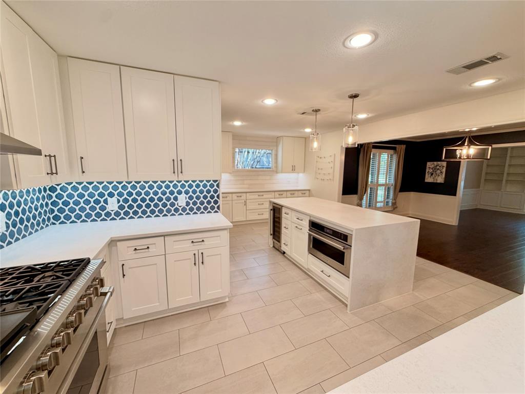 Kitchen featuring white shaker-style cabinetry, a large central island with an integrated beverage refrigerator, light-toned tile flooring, recessed lighting, and a patterned tile backsplash