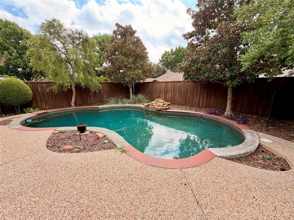 Free-form swimming pool featuring a rock water feature, brick coping, aggregate concrete decking, and a perimeter wood privacy fence