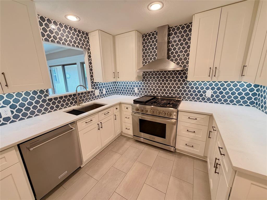 Kitchen featuring white cabinetry, solid-surface countertops, decorative geometric backsplash, stainless steel gas range with overhead vent hood, and neutral-tone tile flooring