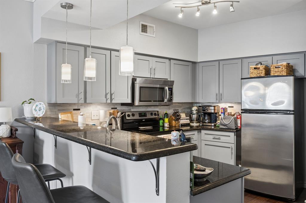 Kitchen featuring gray cabinetry, stainless steel appliances, dark stone countertops, a tile backsplash, and pendant lighting over a breakfast bar