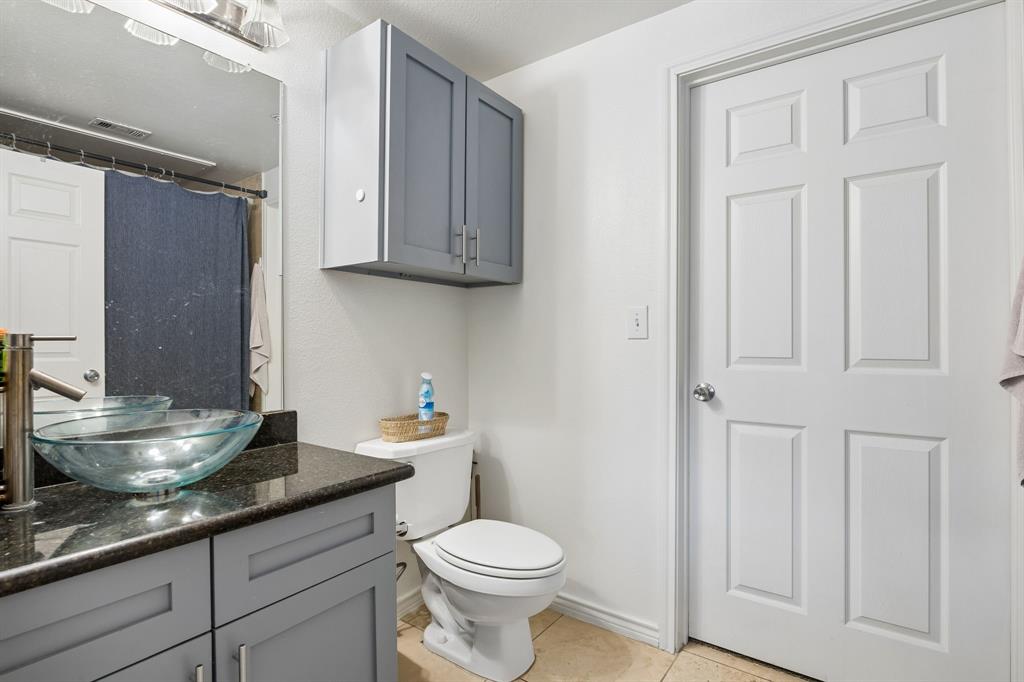Bathroom featuring a vessel sink, dark stone-finish countertop, light gray cabinetry, and neutral tile flooring