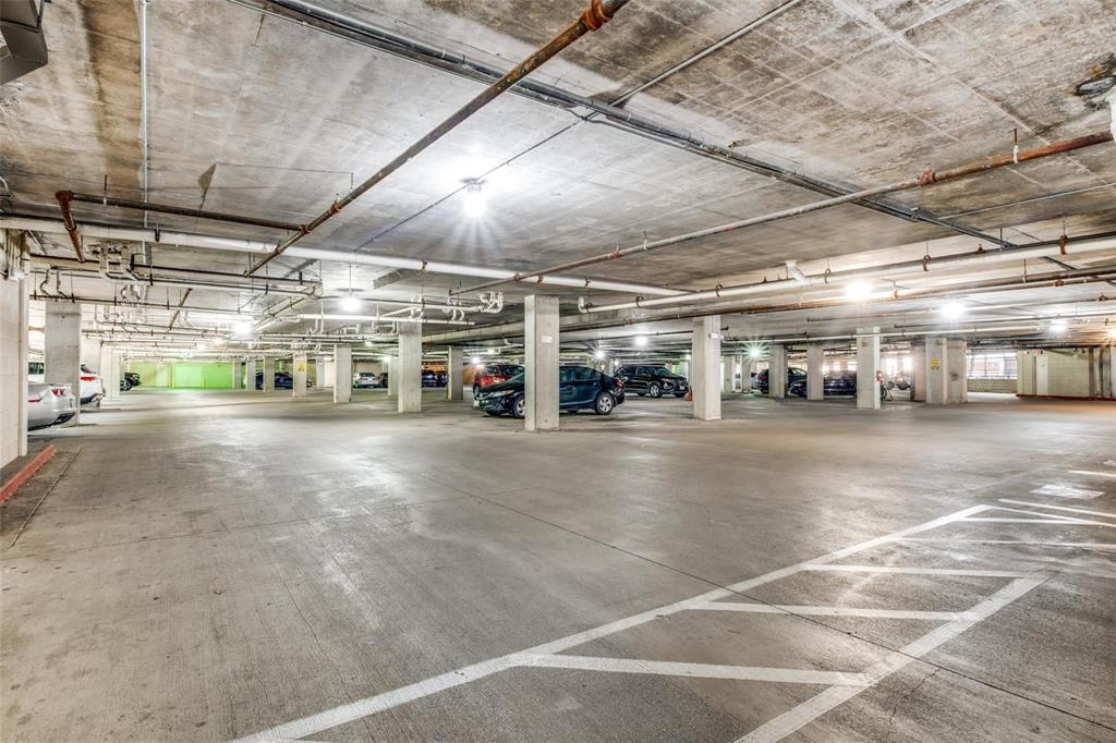 Spacious concrete parking garage with multiple columns, overhead piping, and ceiling-mounted lighting fixtures