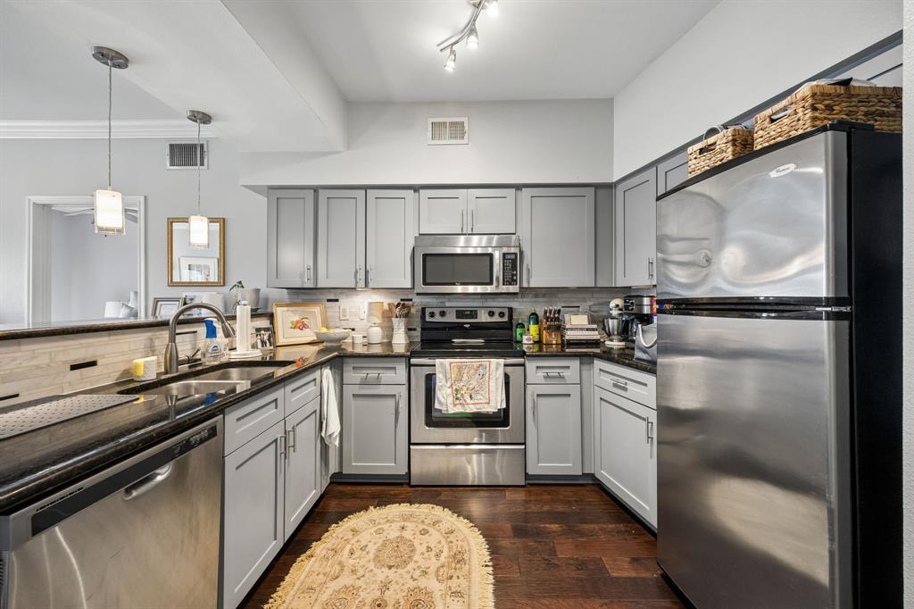 Well-appointed kitchen featuring light gray cabinetry, stainless steel appliances, dark countertops, a tiled backsplash, and recessed and pendant lighting