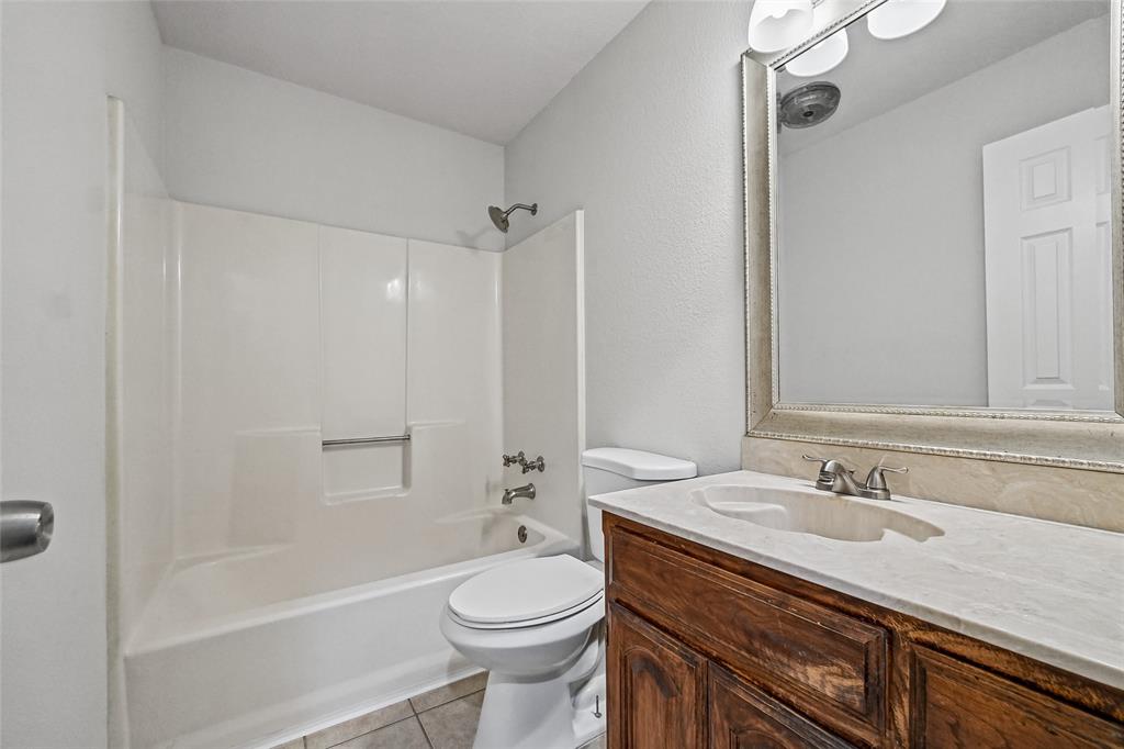 Bathroom featuring a wood-finish vanity with a stone-surface countertop, an integrated sink with a dual-handle faucet, a framed mirror with integrated lighting, and a tub-shower combination with a molded surround