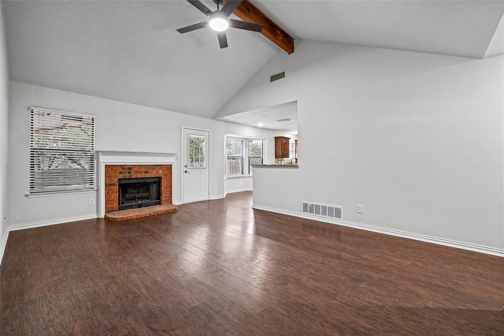 Vaulted ceiling featuring a decorative wood-finish beam, wood-finish flooring, masonry fireplace with a classic mantel, and a ceiling fan with integrated lighting
