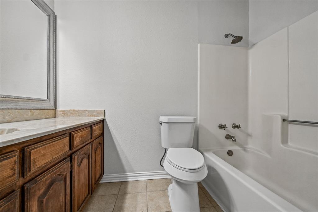 Bathroom featuring a wood vanity with stone countertop, integrated sink, framed wall mirror, and a tub-shower combination with metal fixtures