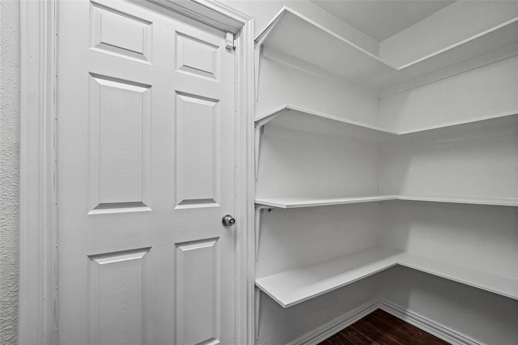 Storage area featuring white paneled door with hardware and multi-level white built-in shelving over wood-finish flooring
