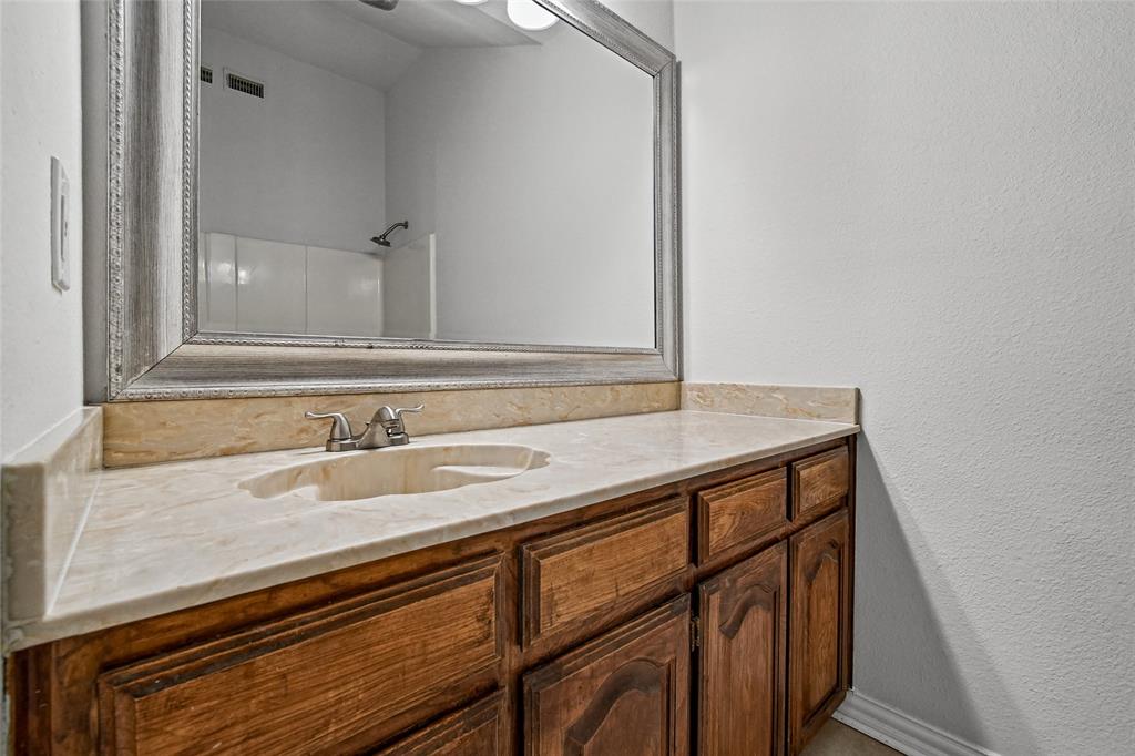 Vanity featuring natural stone-finish countertop, integrated sink, dual-handle faucet, and wood-finish cabinetry topped with a framed mirror