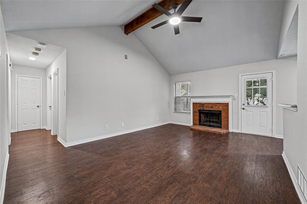 Vaulted ceiling featuring a natural wood-finish beam, wood-finish flooring, masonry fireplace with a mantel, and a multi-light exterior door