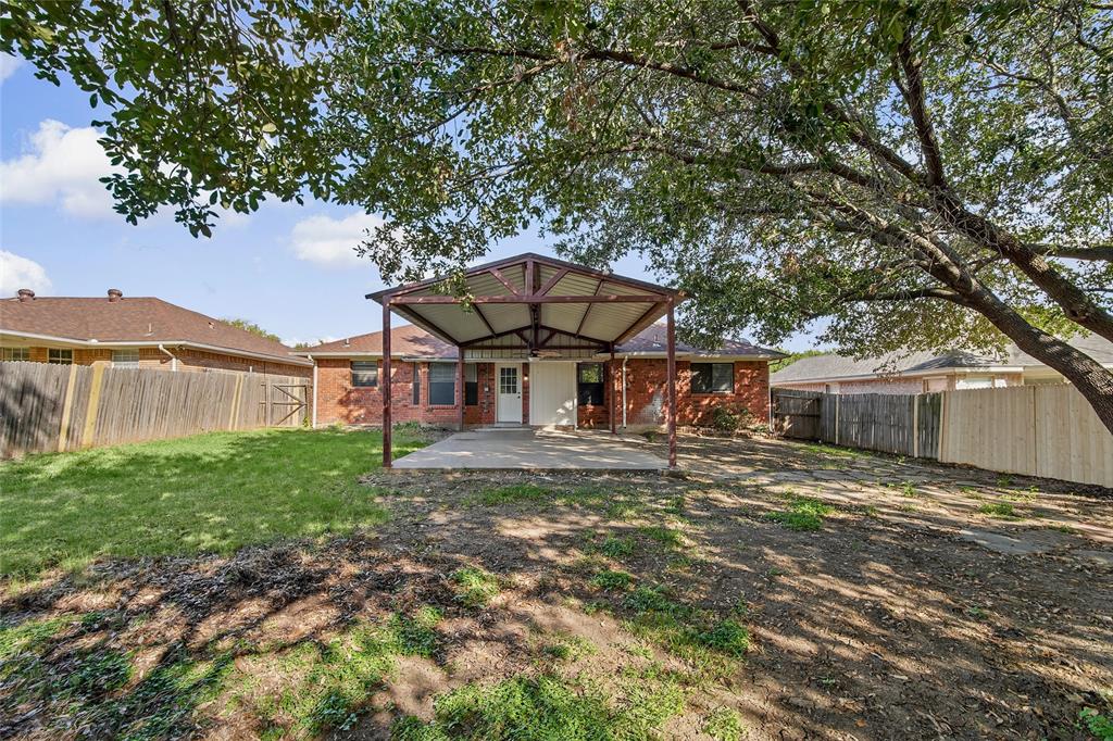 Backyard featuring a covered patio with metal roofing, brick exterior, wood-style perimeter fencing, and mature trees