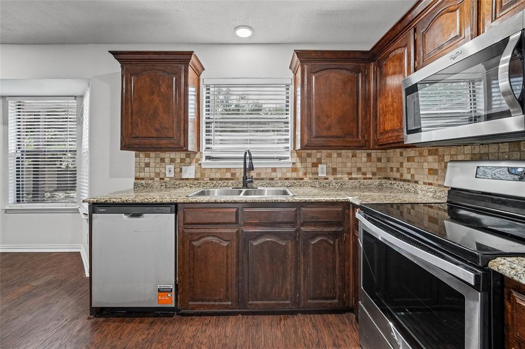 Kitchen featuring stained wood cabinetry, stone-patterned countertops, a tiled backsplash, and stainless steel appliances