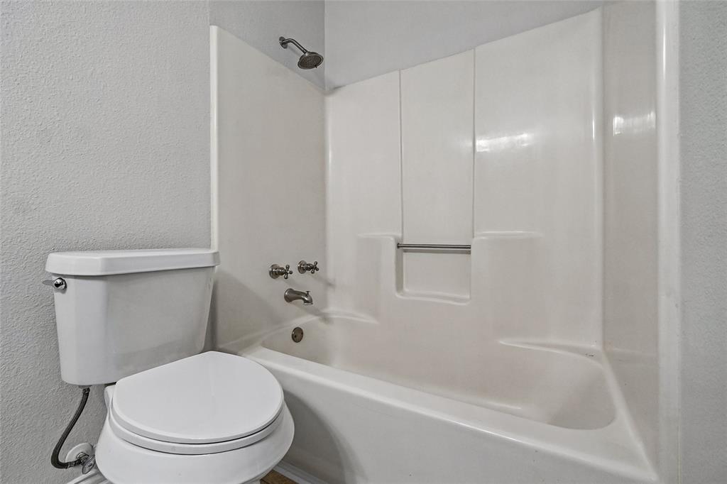 Bathroom featuring a porcelain toilet and an integrated tub and shower combination with a built-in recessed storage shelf and metallic fixtures