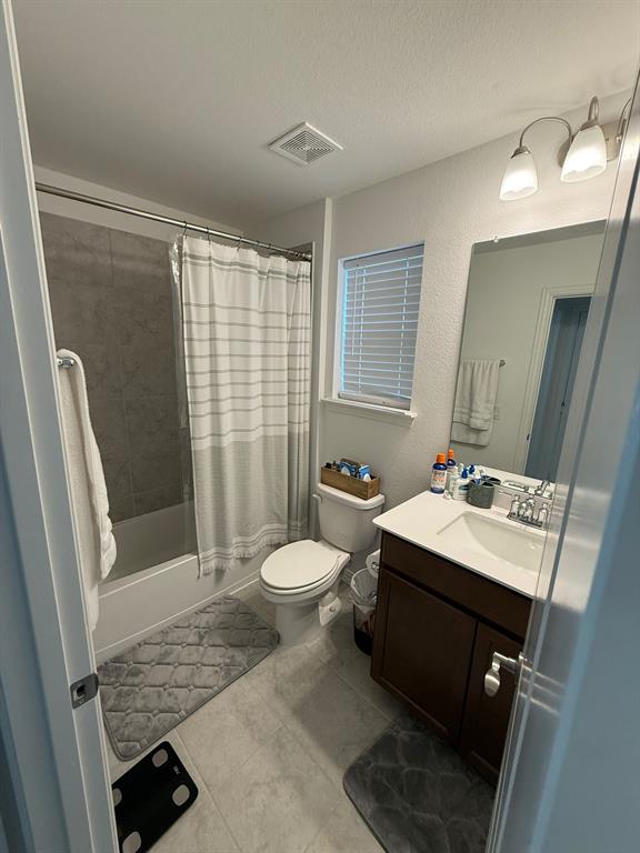 Full bathroom featuring shower / bath combo, vanity, a textured wall, a textured ceiling, and light tile patterned floors