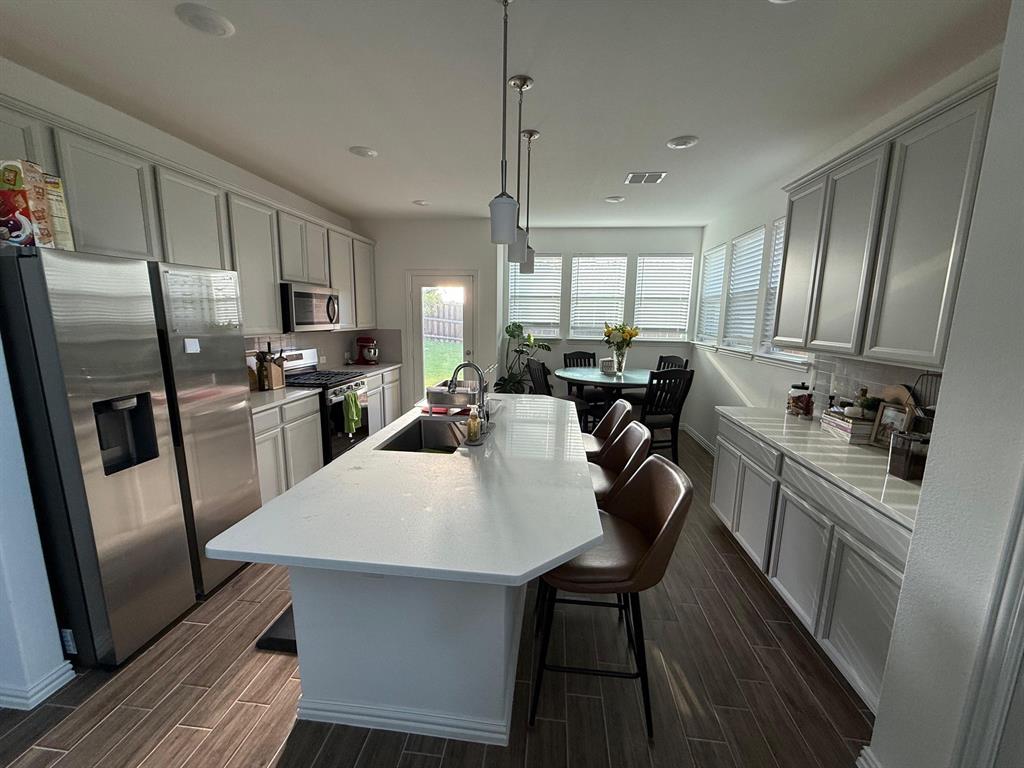 Kitchen with appliances with stainless steel finishes, wood tiled floors, hanging light fixtures, a kitchen breakfast bar, and an island with sink
