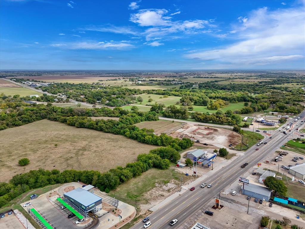 Aerial perspective featuring expansive acreage, mature tree-lined borders, and prominent frontage along a major thoroughfare
