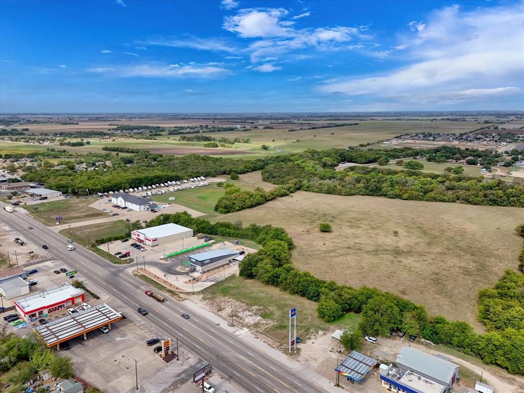 Aerial view of expansive undeveloped acreage featuring direct highway frontage, cleared terrain, and mature tree borders