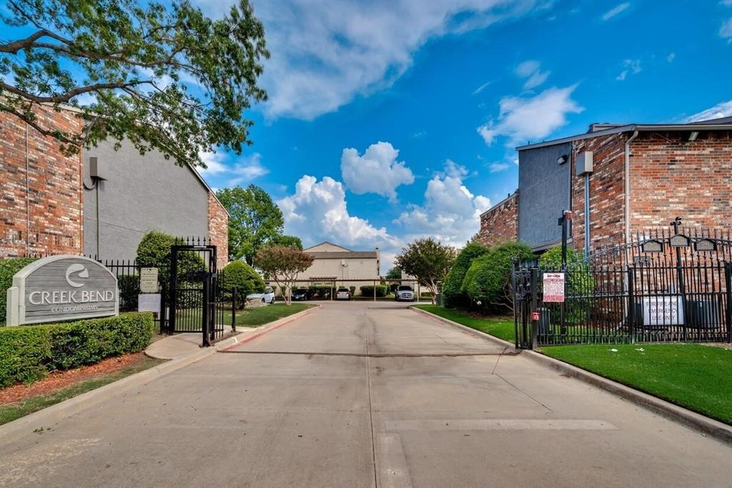 Gated entrance featuring a concrete driveway, perimeter metal fencing, and brick-exterior structures Gated entrance featuring a concrete driveway, perimeter metal fencing, and brick-exterior structures