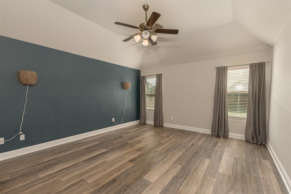 Vaulted ceiling featuring a ceiling fan with integrated lighting, wood-finish flooring, and a decorative accent wall Vaulted ceiling featuring a ceiling fan with integrated lighting, wood-finish flooring, and a decorative accent wall
