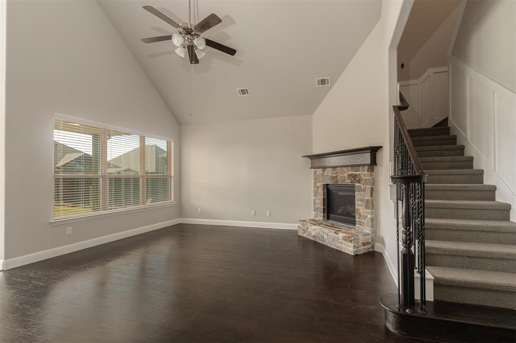 Vaulted ceiling featuring a ceiling fan, stone-surround fireplace with a wooden mantel, wood-finish flooring, and a staircase with a decorative iron balustrade
