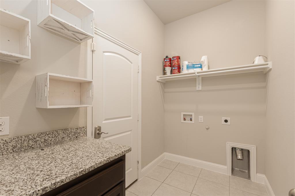 Utility room featuring stone-finish countertops, built-in cabinetry, tile flooring, and a wall-mounted shelving unit