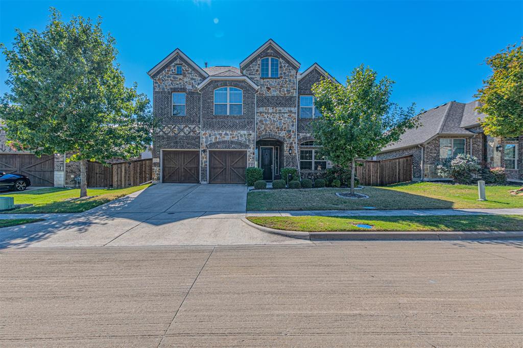 Two-story exterior featuring multi-textured stone and brick masonry, double-gabled roofline, arched window detailing, and carriage-style garage doors Two-story exterior featuring multi-textured stone and brick masonry, double-gabled roofline, arched window detailing, and carriage-style garage doors