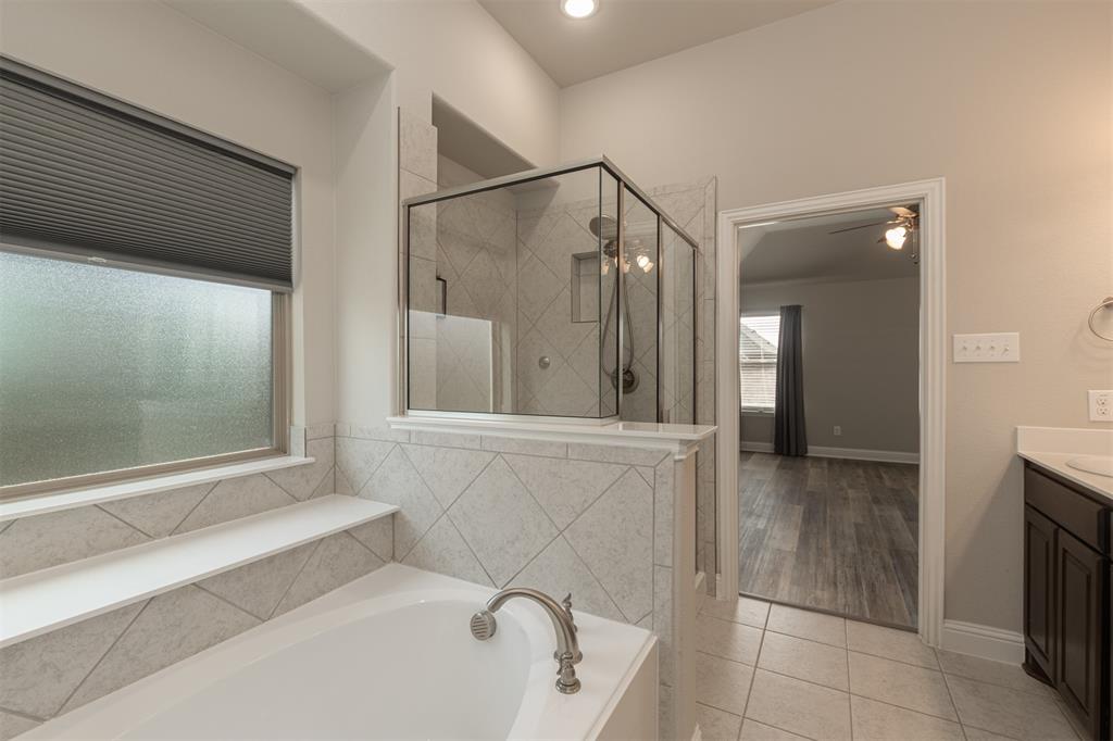 Soaking tub featuring a deck-mounted brushed nickel faucet, separate glass-enclosed shower with tiled surround, and high ceilings