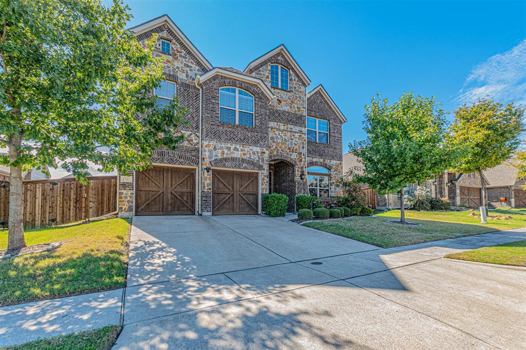 Two-story exterior featuring a stone and brick facade, arched window detailing, and dual carriage-style garage doors Two-story exterior featuring a stone and brick facade, arched window detailing, and dual carriage-style garage doors