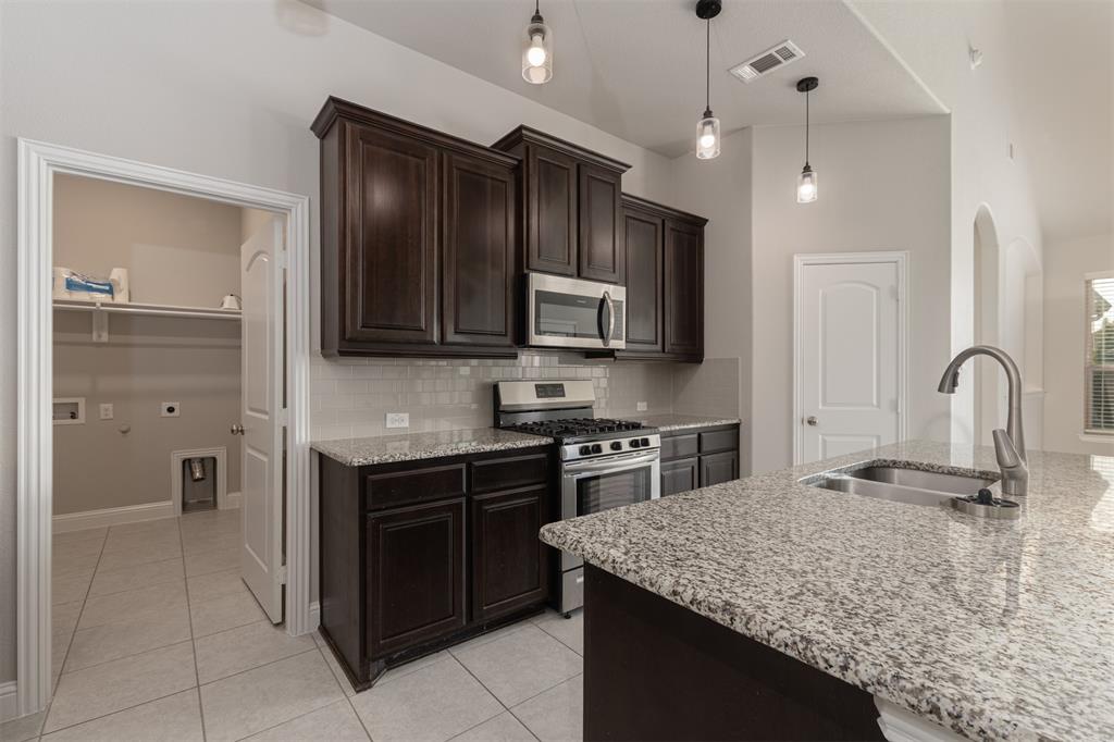 Kitchen featuring dark wood cabinetry, stone countertops, stainless steel appliances, tile backsplash, and pendant lighting