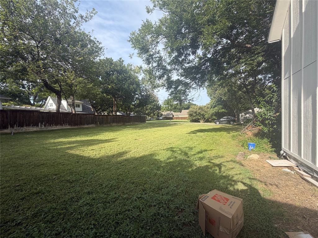 Expansive backyard featuring a large grass lawn, mature trees, and wooden perimeter fencing